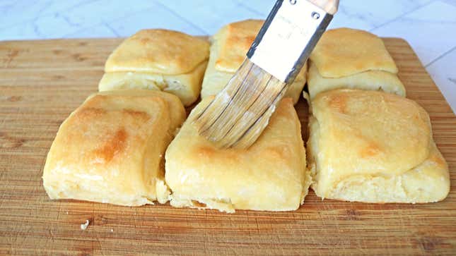 Brush buttering dinner rolls.
