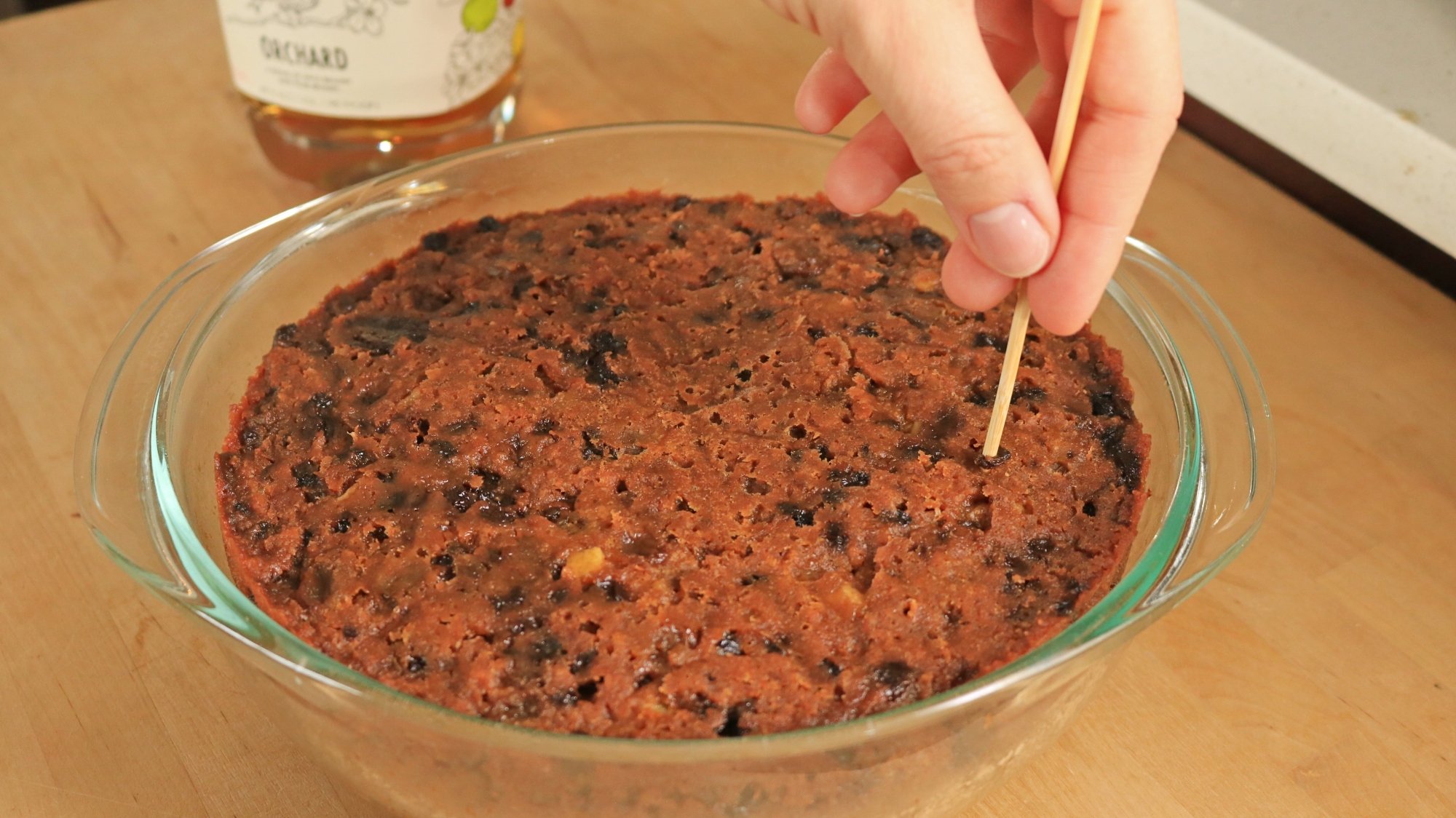 Hand using wood skewer to poke a hole into a cake.