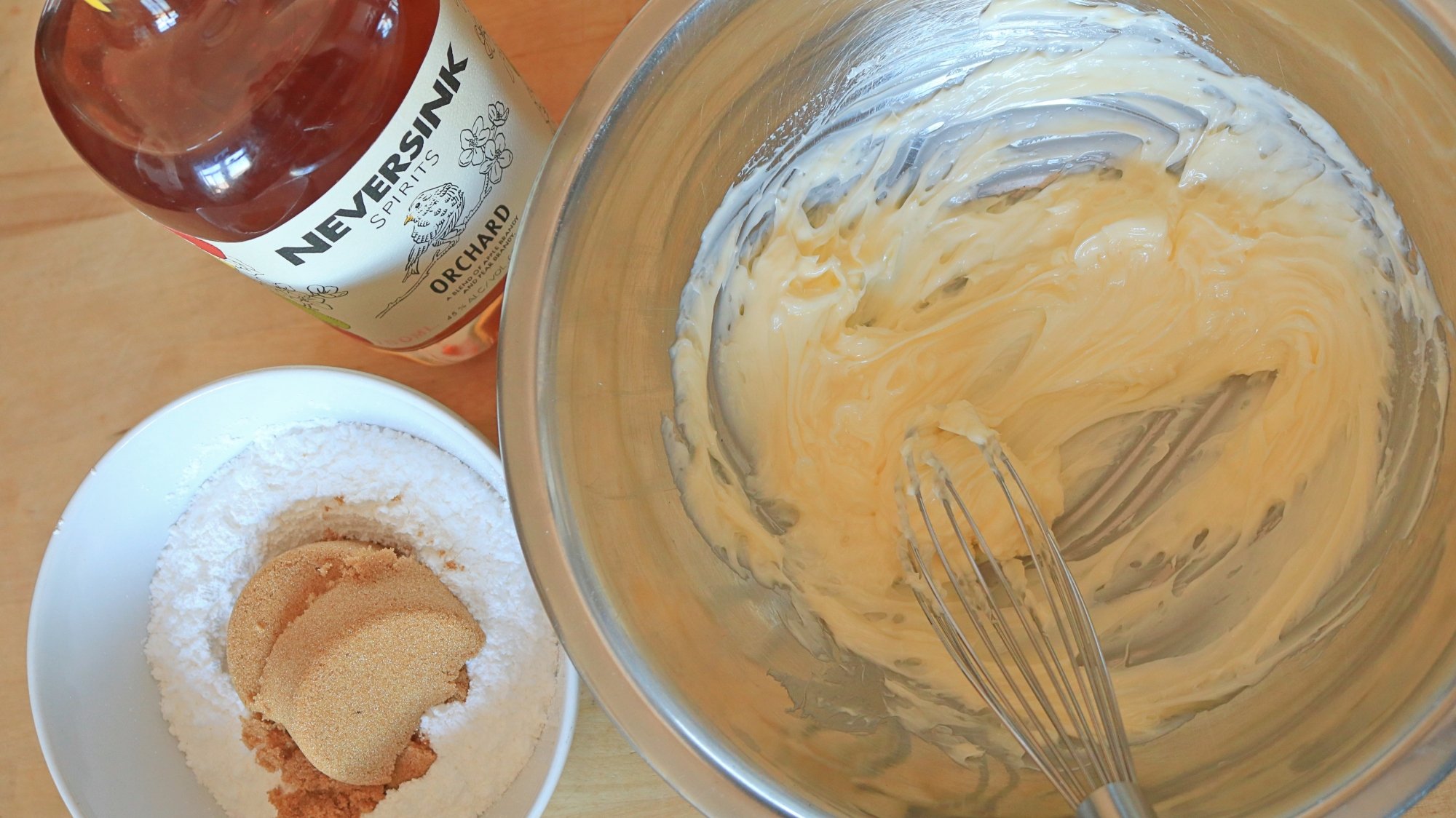 A bowl of butter next to a bowl of sugar and a bottle of brandy.