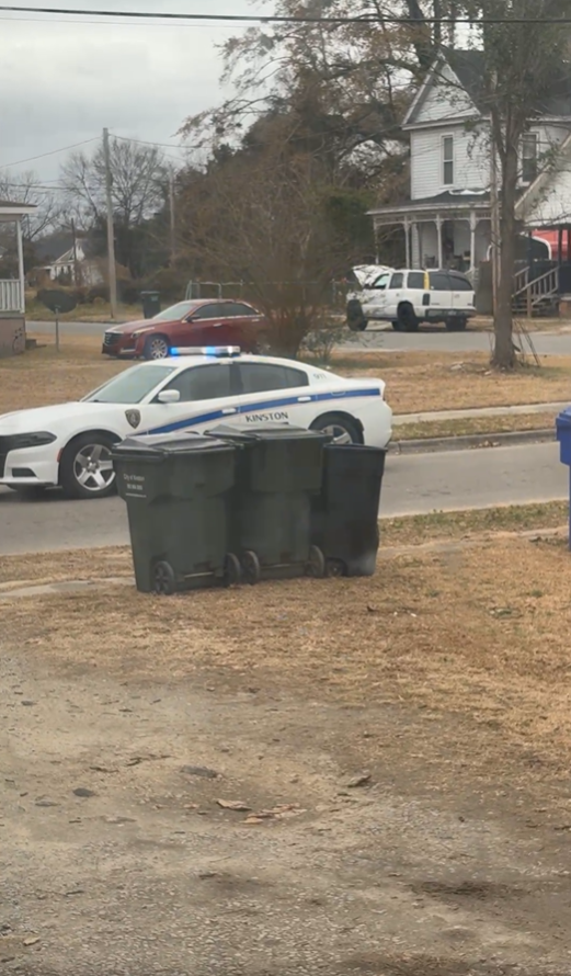 Kinston police vehicles are parked along a residential street near a house during an active police response.