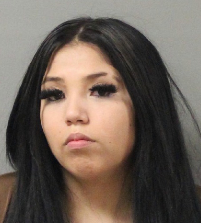 Mugshot-style photo of Tashawana Tuckta with long dark hair, heavy eyelashes, and a neutral expression, photographed against a light background.