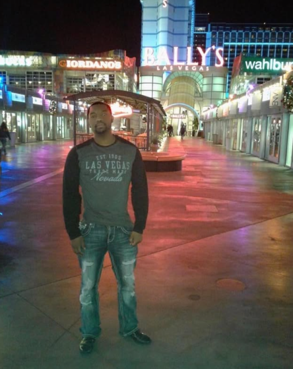 Shaun Joseph Benward stands on an illuminated outdoor promenade at night in front of Bally’s Las Vegas, with Giordano’s and Wahlburgers signs glowing in the background.